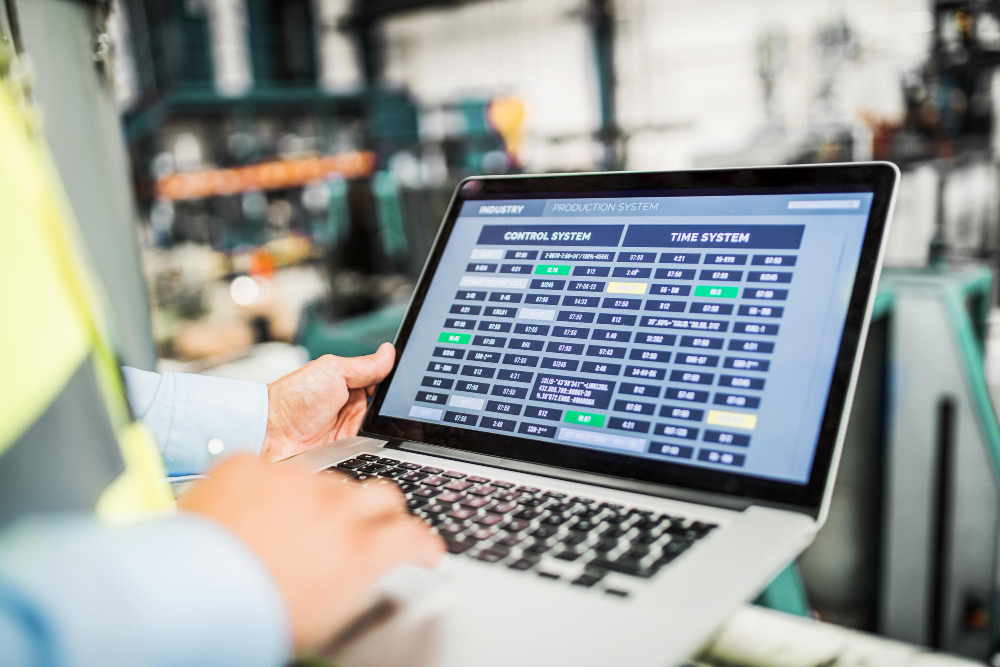 Operator monitoring factory operations using digital manufacturing software on a laptop in an industrial environment.